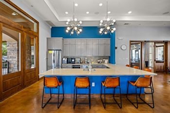 A kitchen with a blue backsplash and a bar area with orange chairs.